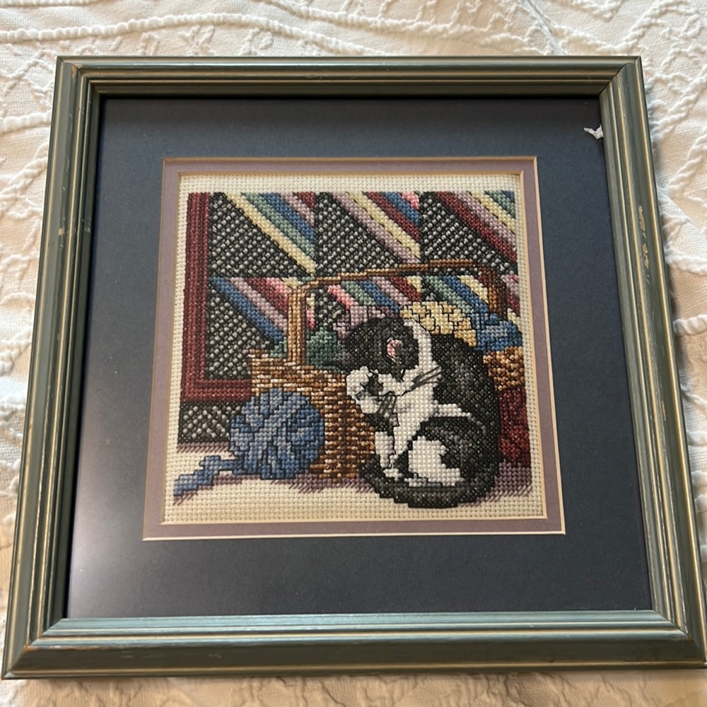 Handmade cross stitching cat with quilt in background.
